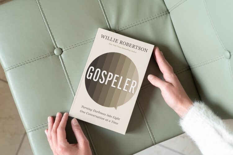 Gospeler by Willie Robertson on a green leather tufted chair with two hands touching the corners of the book lightly